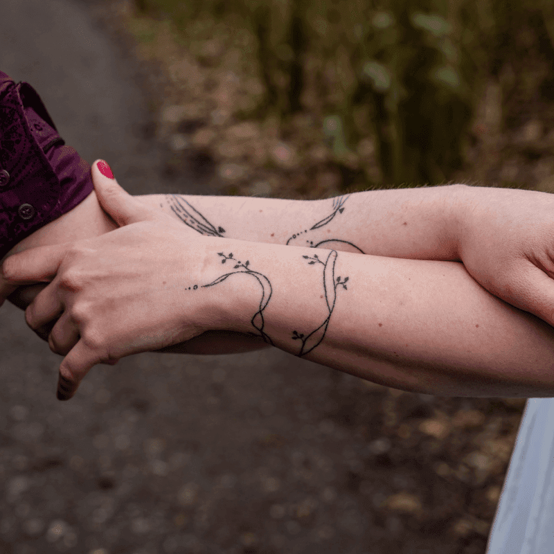 Twee bijpassende fineline takken met bladeren op onderarmen.