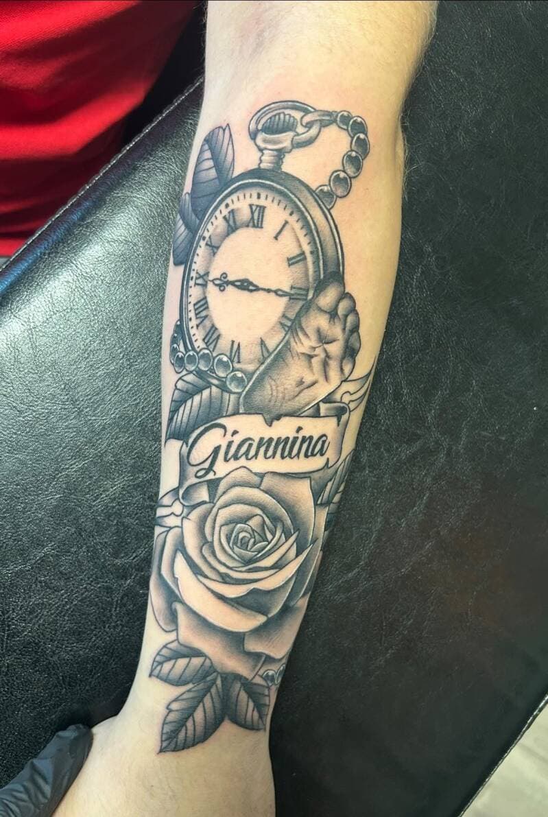 Blackwork tattoo van een zakhorloge, babyvoetje, roos en de naam 'Giannina'.