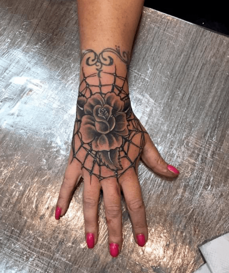 Zwart-wit roos in spinnenweb op hand, met sierlijke polsband.