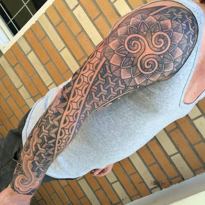 Grote sleeve tattoo met geometrische patronen, dotwork en een triskele symbool.