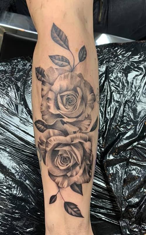 Realistische zwart-wit tattoo van twee rozen met bladeren op het onderbeen.