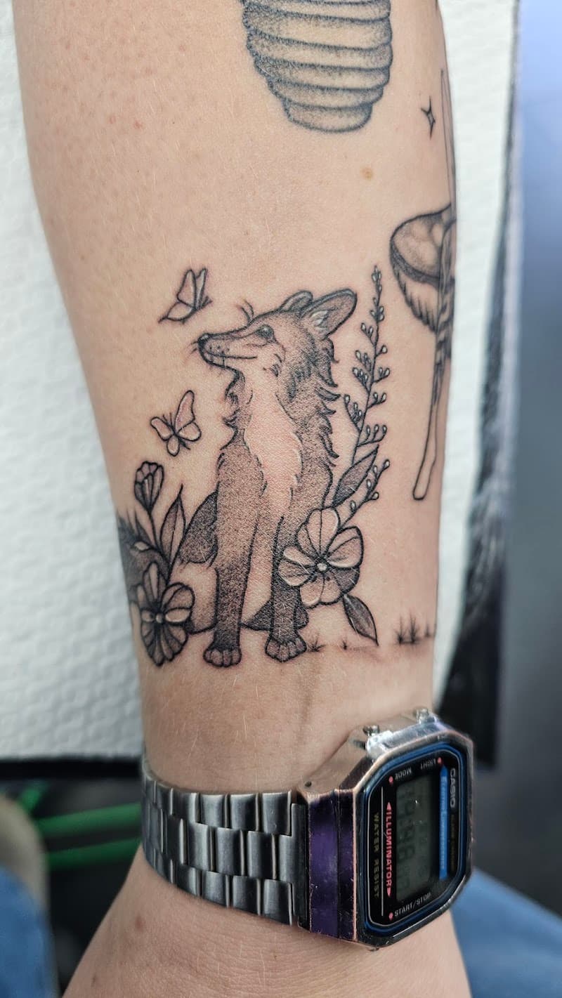 Zwart-grijze tattoo van een vos met bloemen en vlinders op de onderarm.