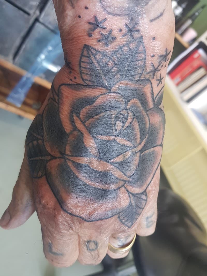 Zwart-grijze roos tattoo op hand met sterren en vingertattoos.