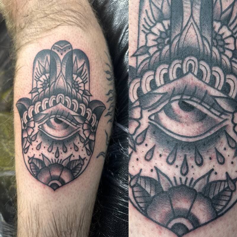 Zwart-wit Hamsa hand met oog en bloemen op onderbeen.
