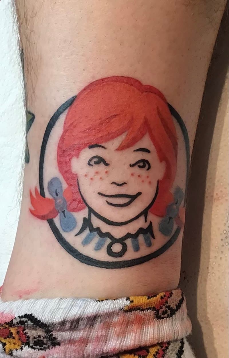 Kleurrijke Wendy's logo tattoo op het onderbeen.