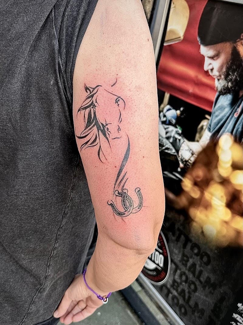 Minimalistische paardenhoofd en hoefijzers tattoo op bovenarm.