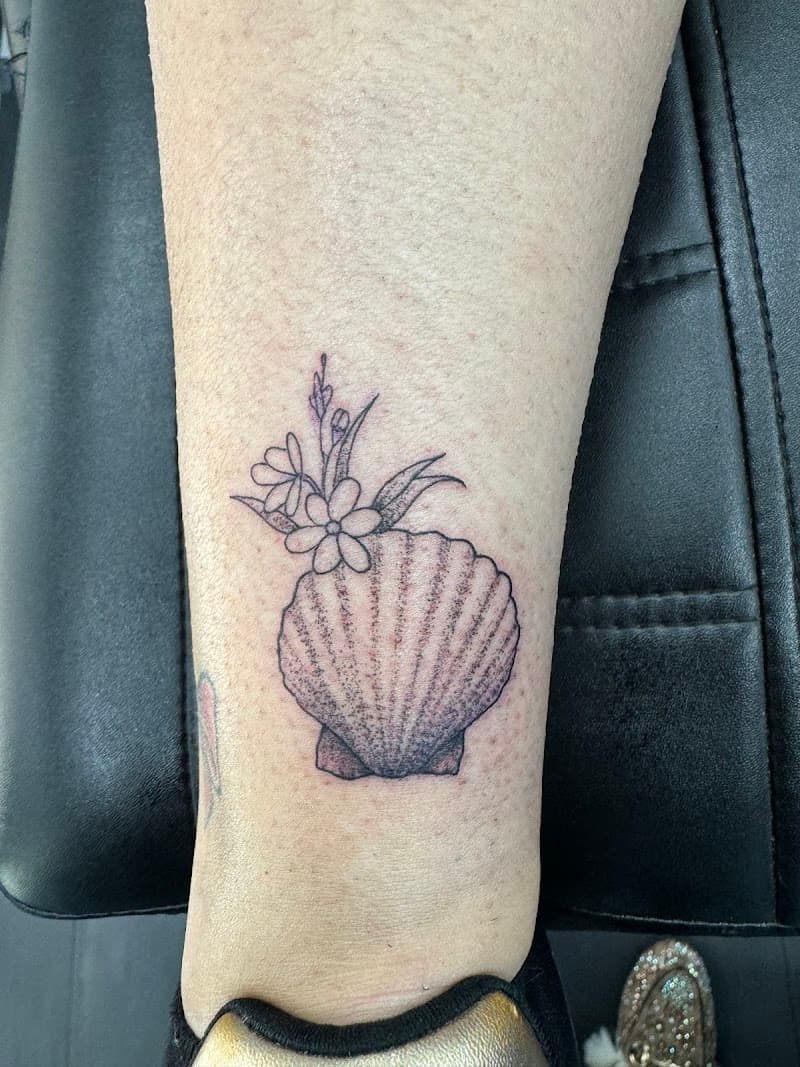 Fineline tattoo van een schelp met bloemen op de enkel.