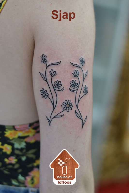 Fineline bloemen en bladeren tattoo op de bovenarm.