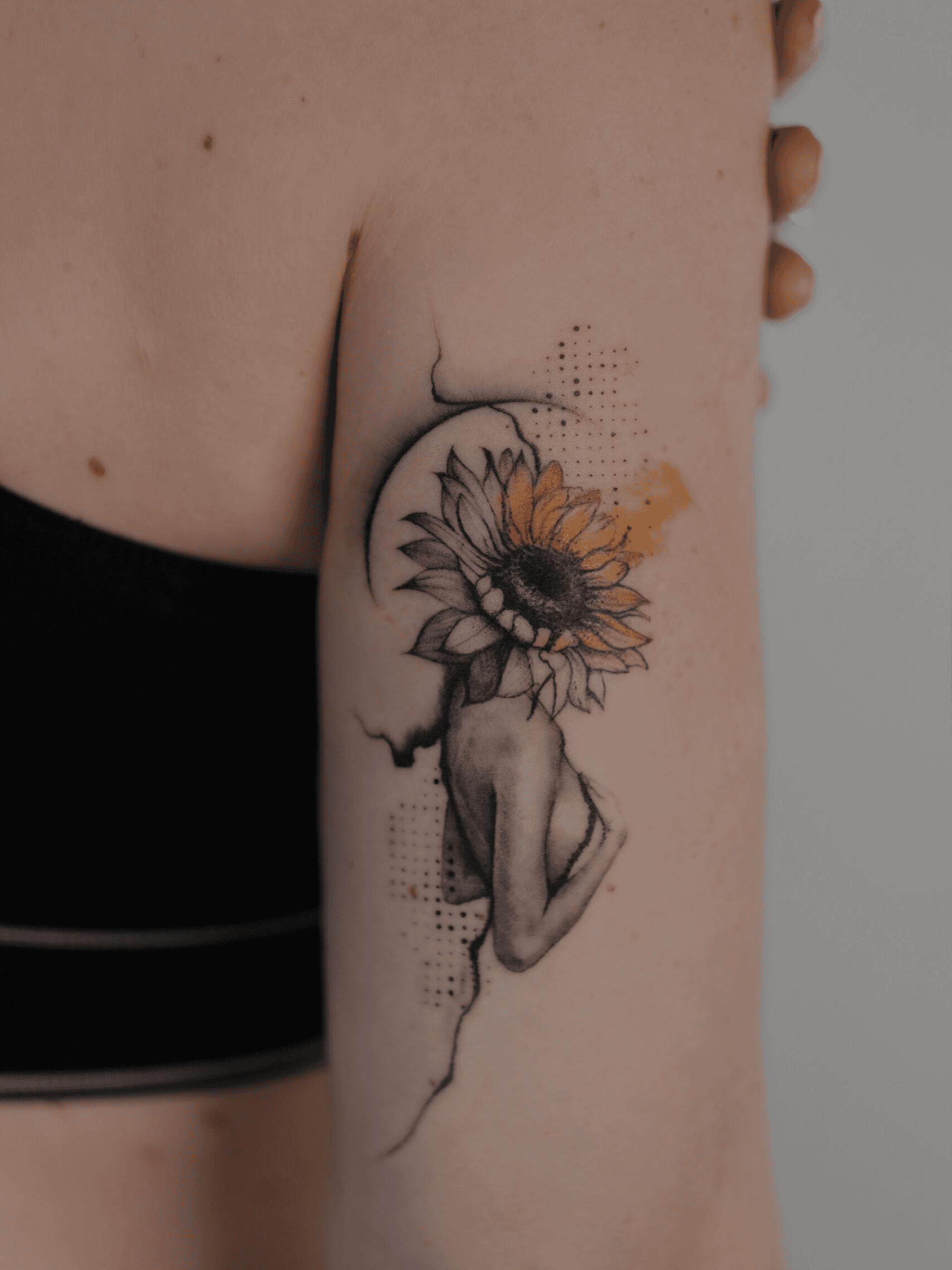 Surrealistische tattoo van vrouw met zonnebloemhoofd op bovenarm.