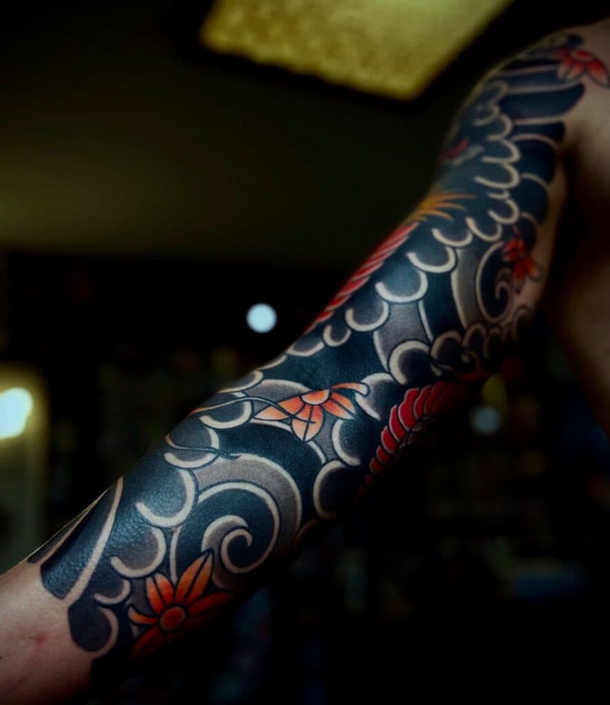 Japanse sleeve tattoo met golven en rode bloemen.