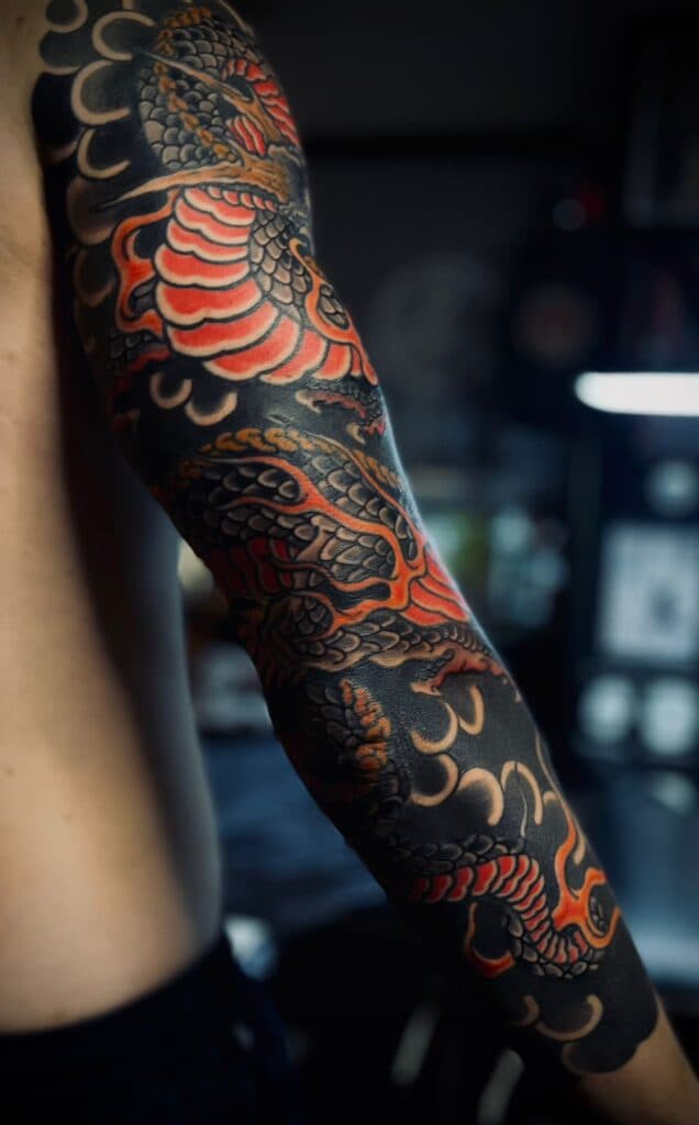 Japanse draak sleeve tattoo in zwart, grijs en rood op de arm.