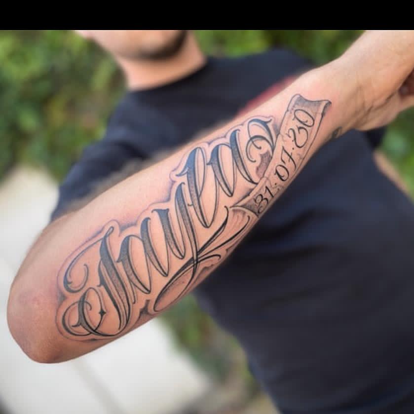 Grote naam 'Jaylen' in sierlijke letters met datum op onderarm.