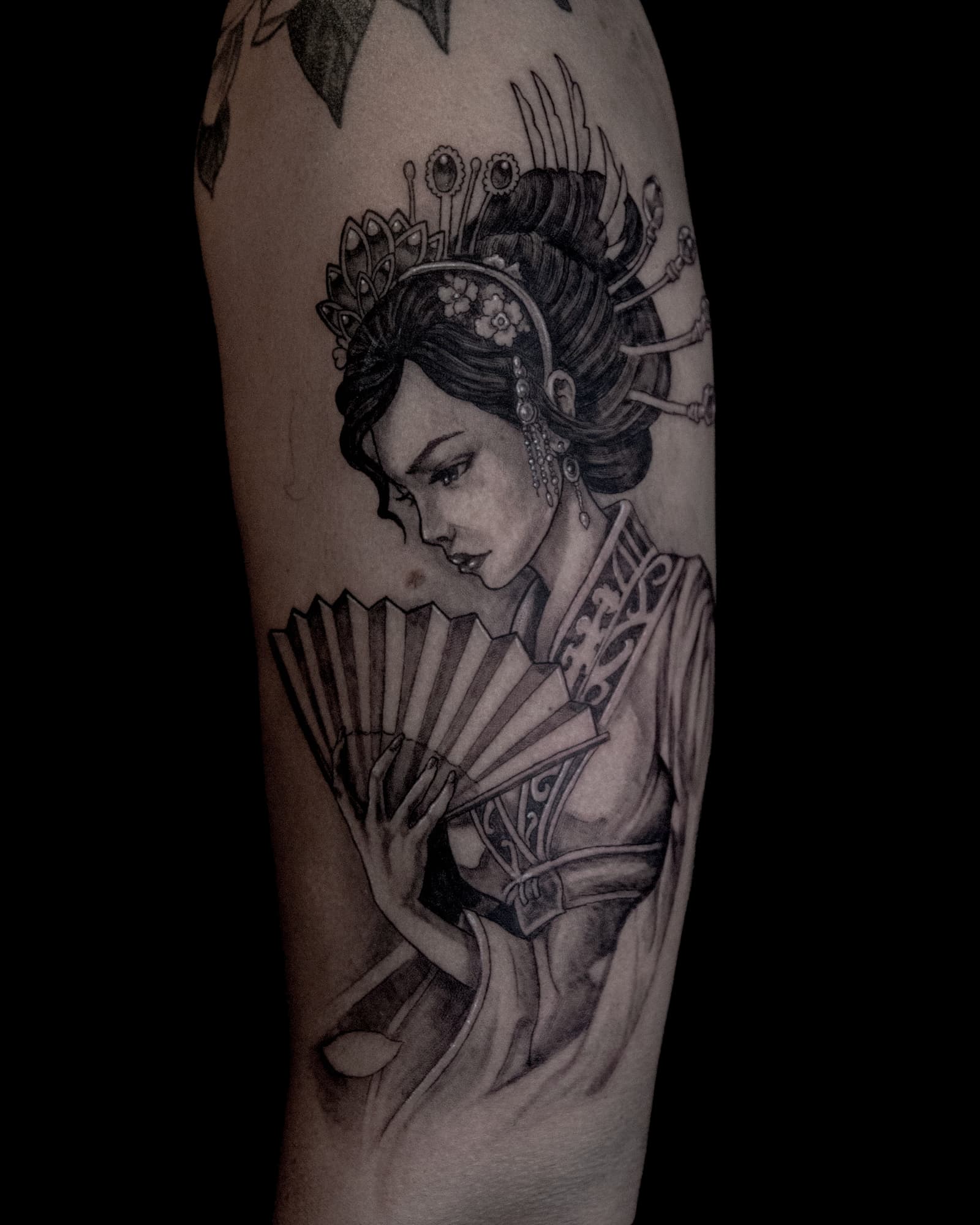 Zwart-wit tattoo van een Geisha met waaier op de bovenarm.
