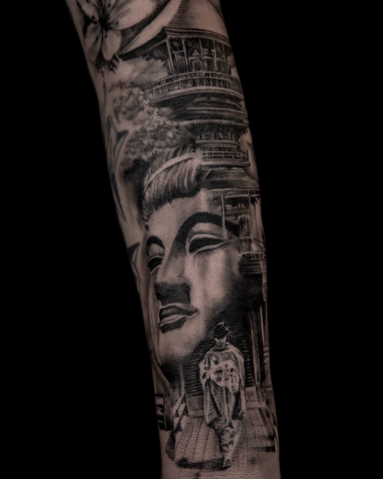 Realistische zwart-wit tattoo van Boeddha, tempel en geisha op een arm.