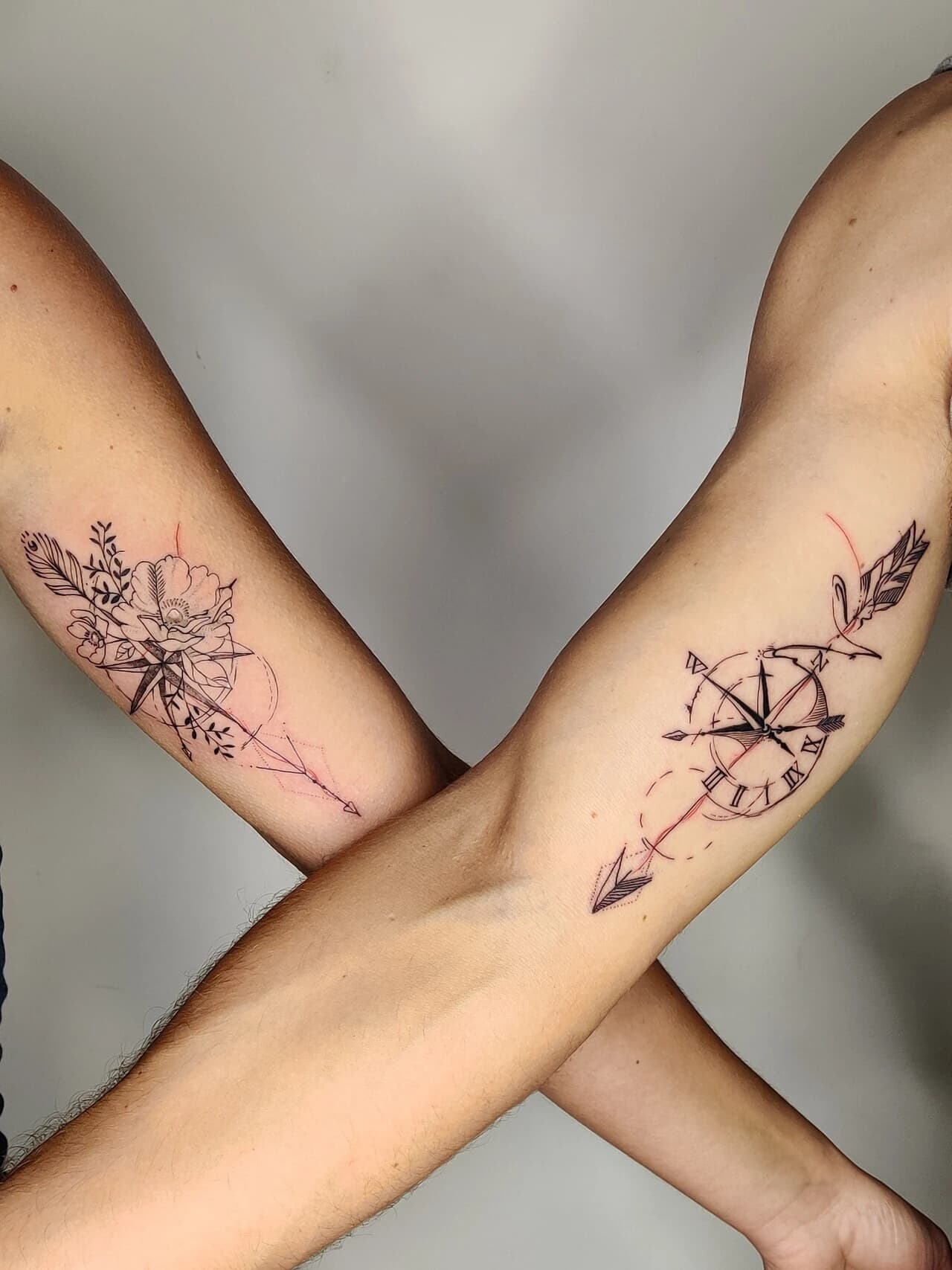 Twee fineline kompas tattoos met bloemen en pijl op onderarmen.