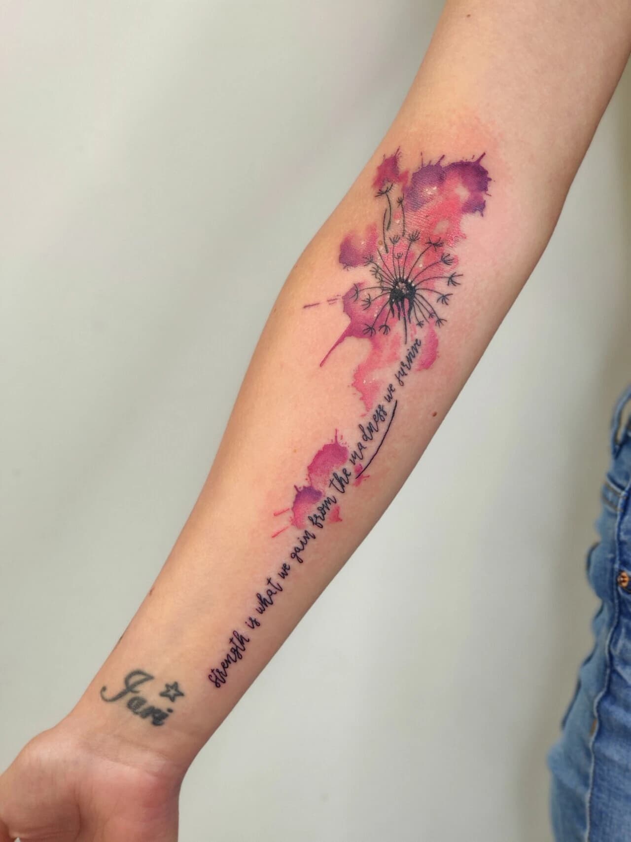 Paardenbloem met tekst en roze/paarse aquarel op onderarm.