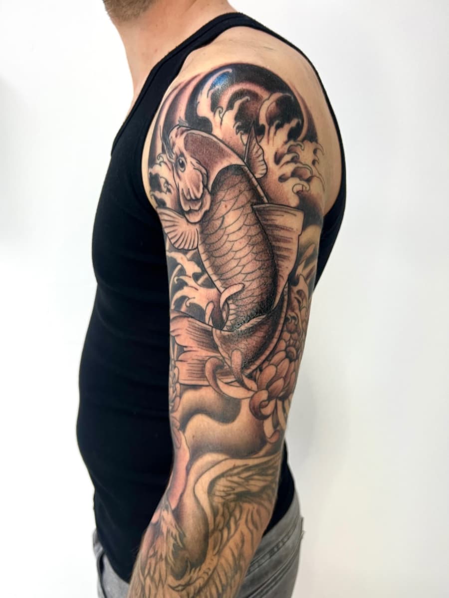 Zwart-wit Japanse koi karper en golven op bovenarm.