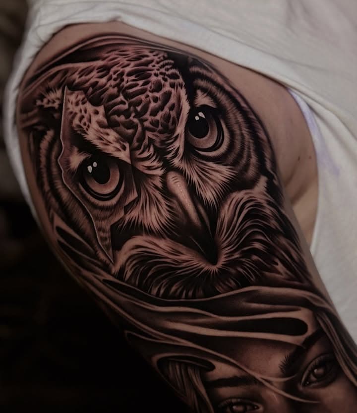 Realistische zwart-wit tattoo van een uil en een vrouwenportret op de bovenarm.