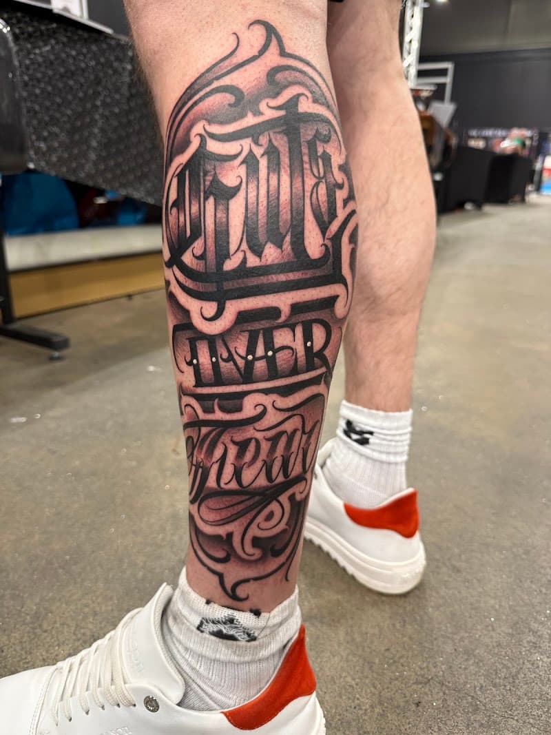 Grote 'Guts Over Fear' lettering tattoo op kuit.