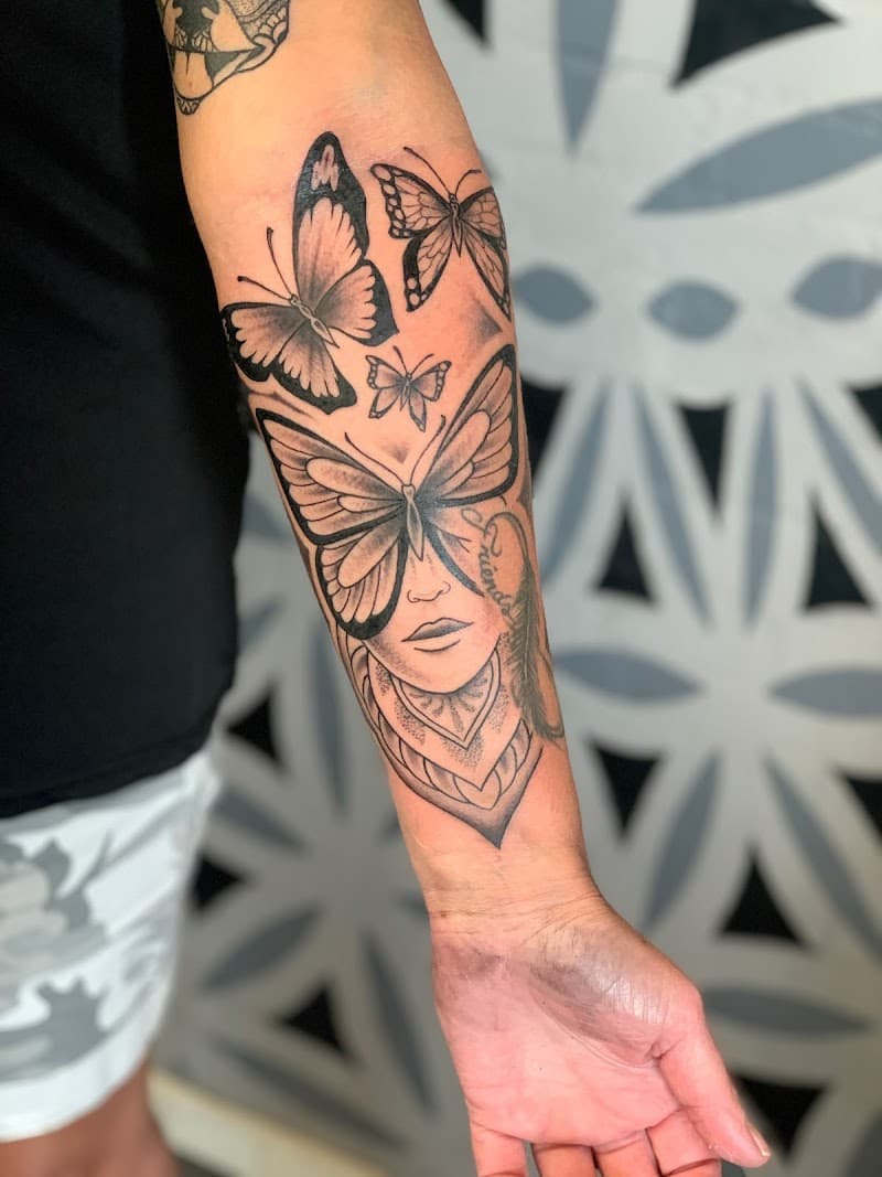 Zwart-wit tattoo van een vrouwengezicht met vlinders en een veer op de onderarm.