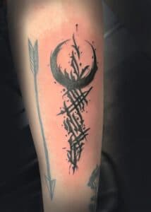 Abstracte zwarte maan en schrift tattoo op onderarm.