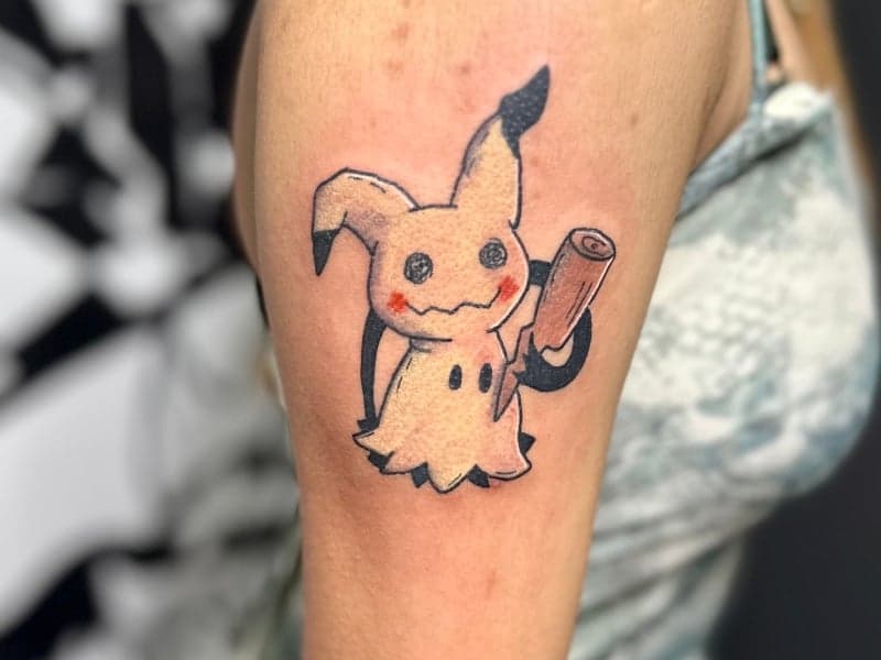 Kleurrijke Mimikyu Pokémon tattoo op bovenarm.