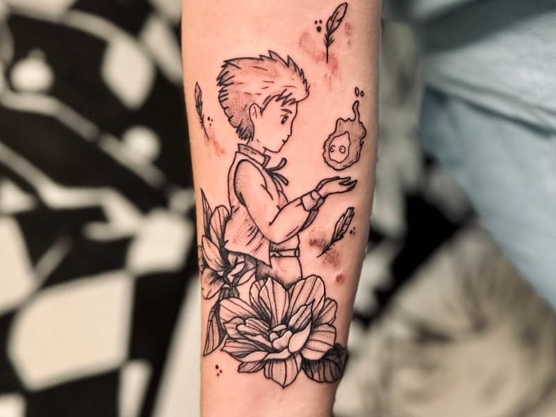 Illustratieve tattoo van Howl en Calcifer met bloemen op onderarm.