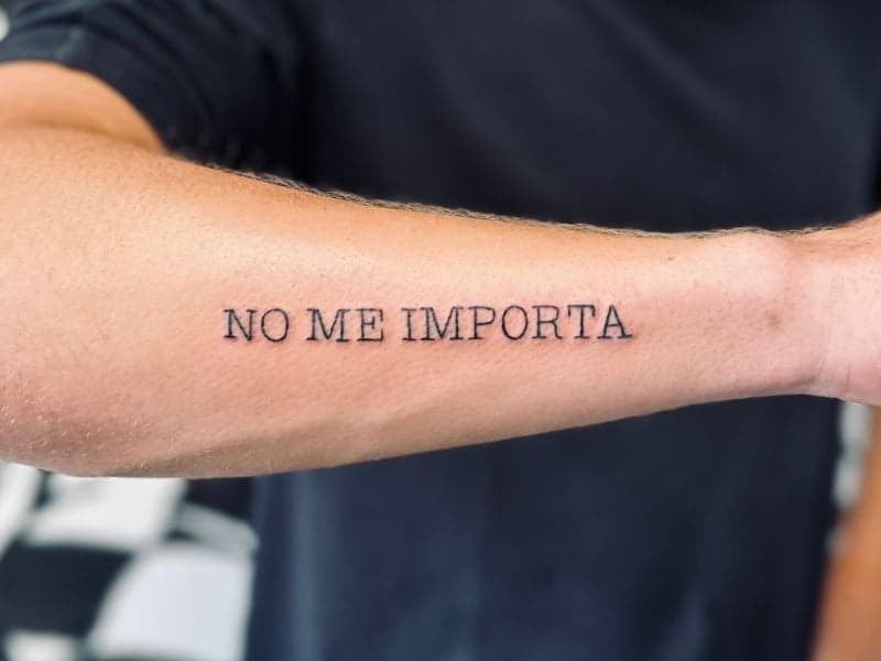 Tekst tattoo 'NO ME IMPORTA' op onderarm in strak lettertype.