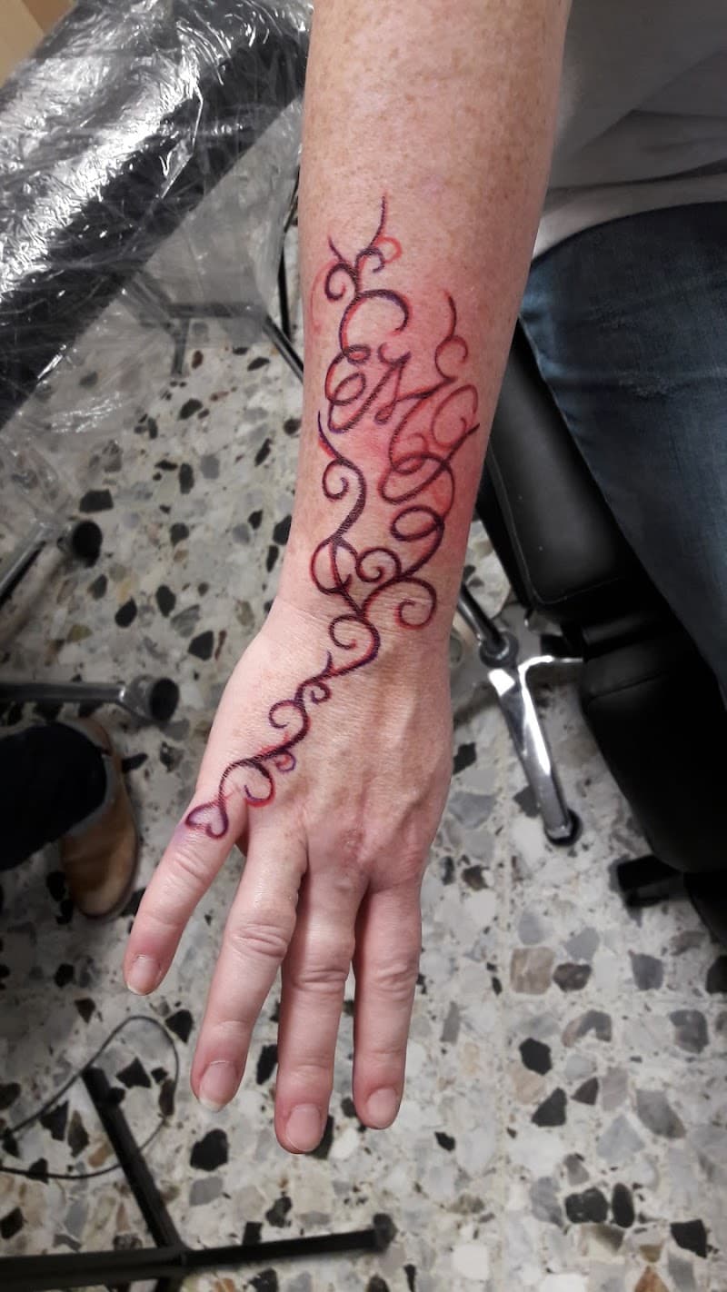 Sierlijke abstracte krullen tattoo in rood/paars op onderarm en hand.