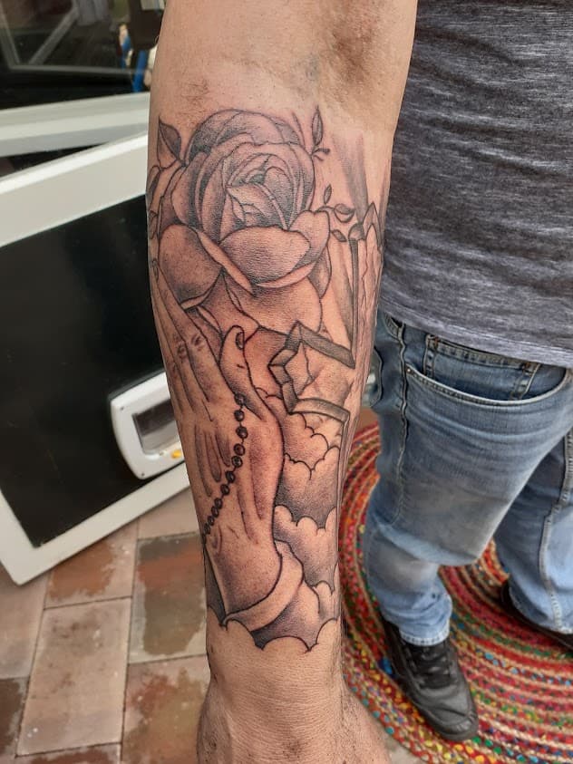 Biddende handen met rozenkrans en roos op onderarm.