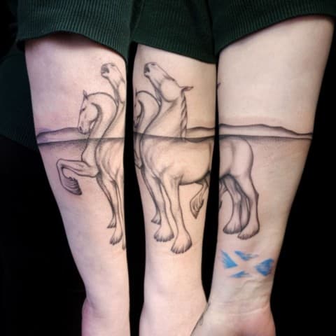 Illustratieve tattoo van twee paarden half in water op onderarm.