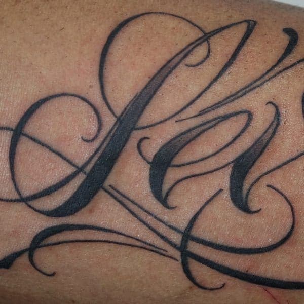 Close-up van sierlijke zwarte script tattoo met de letters 'Pa'.
