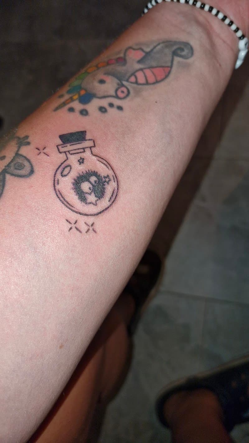 Drie kleine tattoos op onderarm: eenhoorn, toverdrankflesje en vlinder.