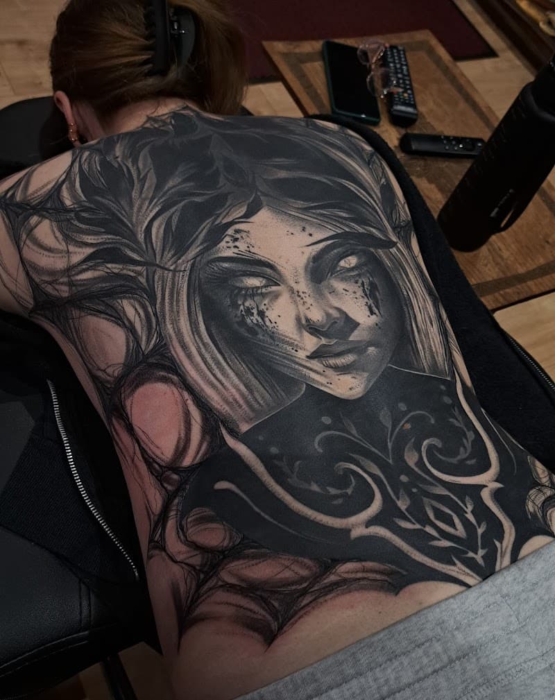 Grote zwart-wit rugtattoo van een vrouwengezicht met duistere, organische elementen.