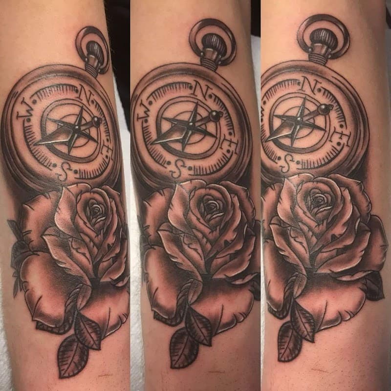 Zwart-wit tattoo van een kompas en een roos op de onderarm.