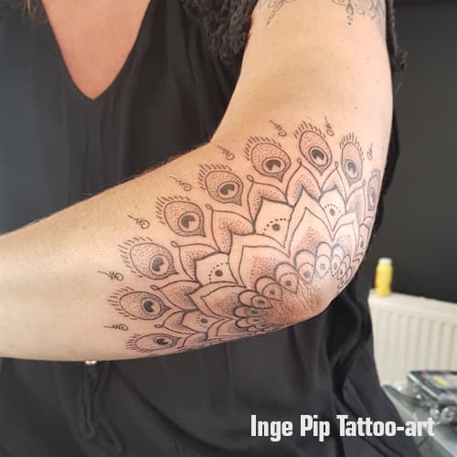 Grote mandala tattoo met pauwenveren op de elleboog, gezet in dotwork stijl.