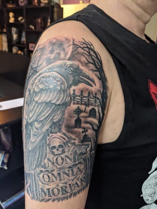 Zwart-wit tattoo van een raaf op een grafsteen met de tekst 'NON OMNIA MORIAR'.