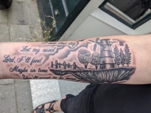 Zwart-wit tattoo van een molen op een zwevend eiland met bijpassende tekst.