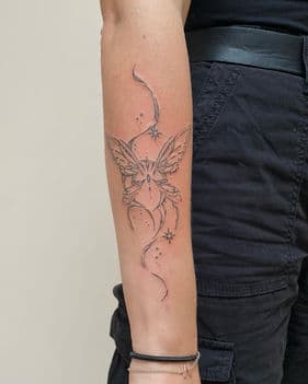 Fineline vlinder met sierlijke lijnen en sterretjes op de onderarm.
