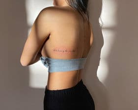 Fijne tekst tattoo op de ribben en ruggengraat.