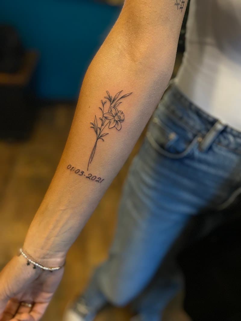 Fineline bloem met datum op onderarm.