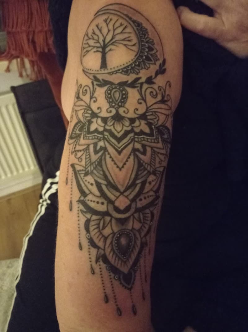 Ornamentale mandala tattoo met levensboom en maan op bovenarm.