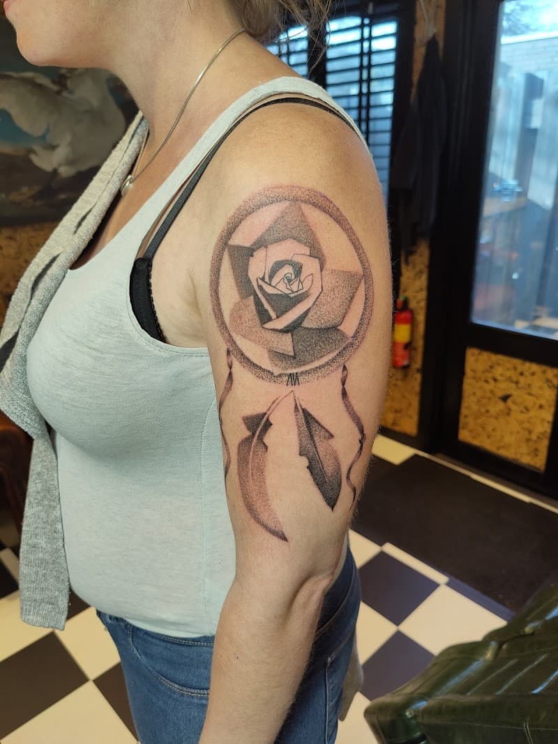 Dotwork dromenvanger met geometrische roos en veren op bovenarm.