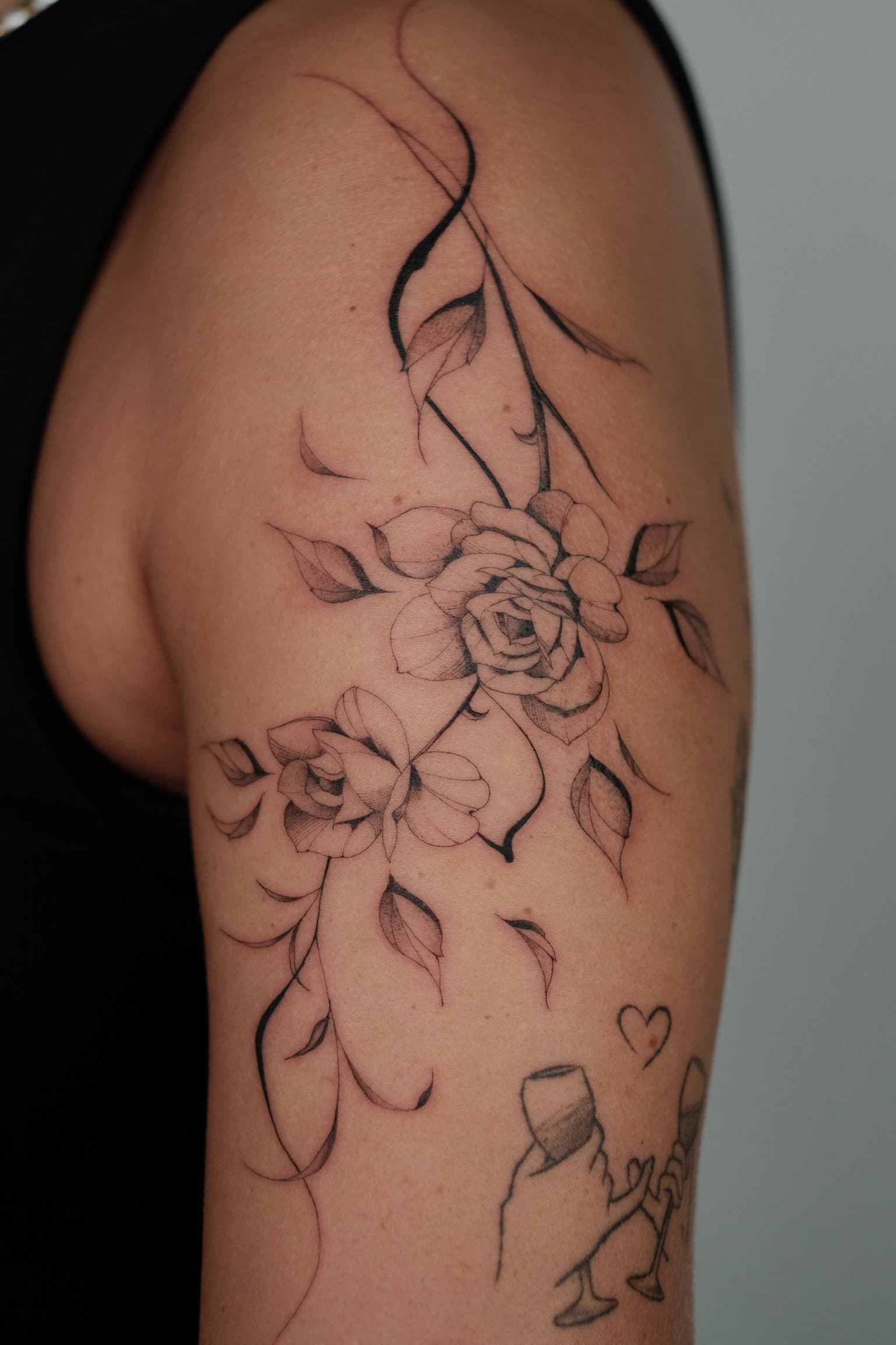 Fineline bloemenrank met rozen op bovenarm.
