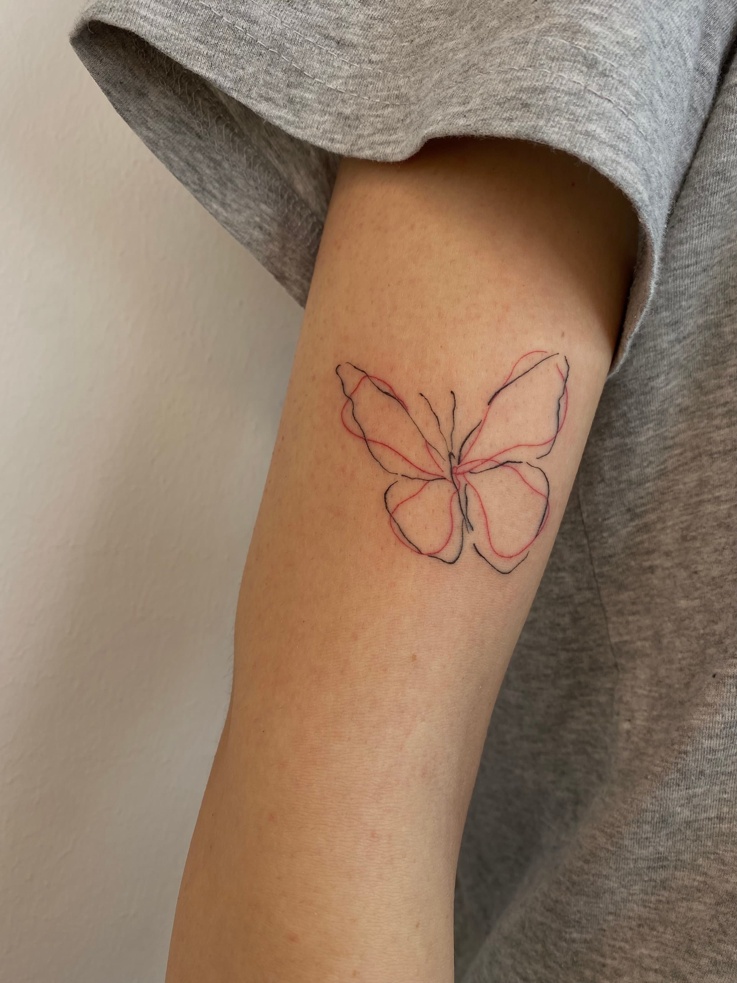 Minimalistische vlinder tattoo met zwarte en rode lijnen op de bovenarm.