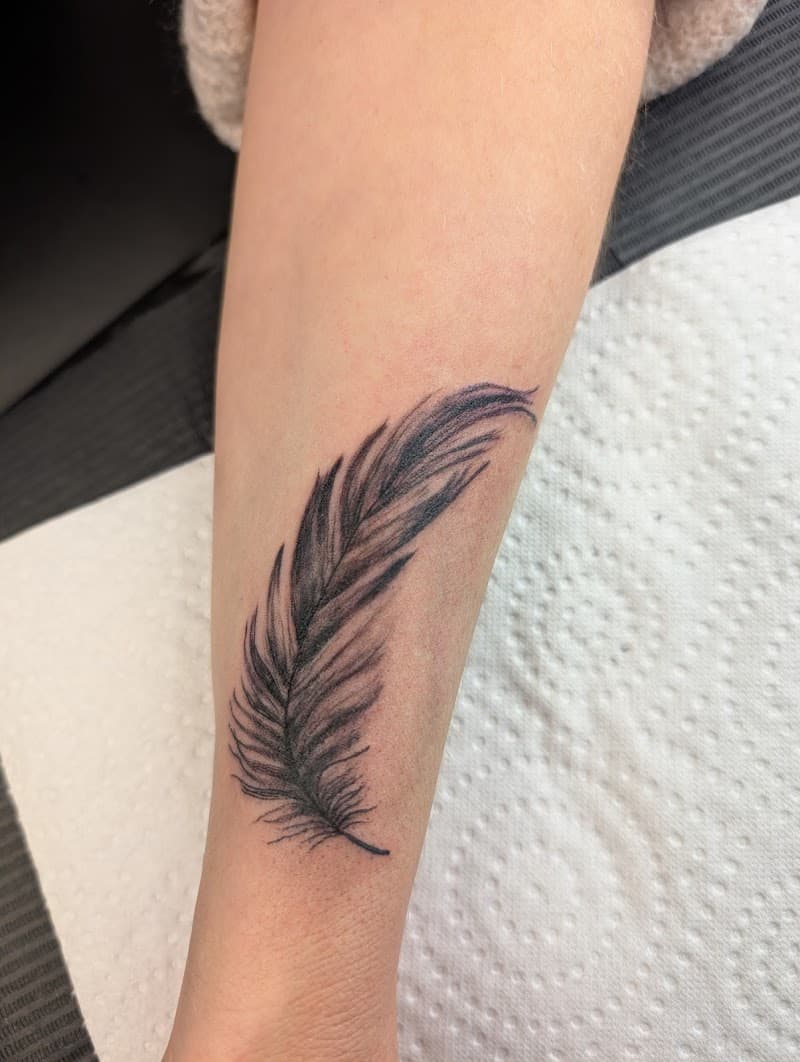 Zwart-grijze illustratieve veer tattoo op de onderarm.