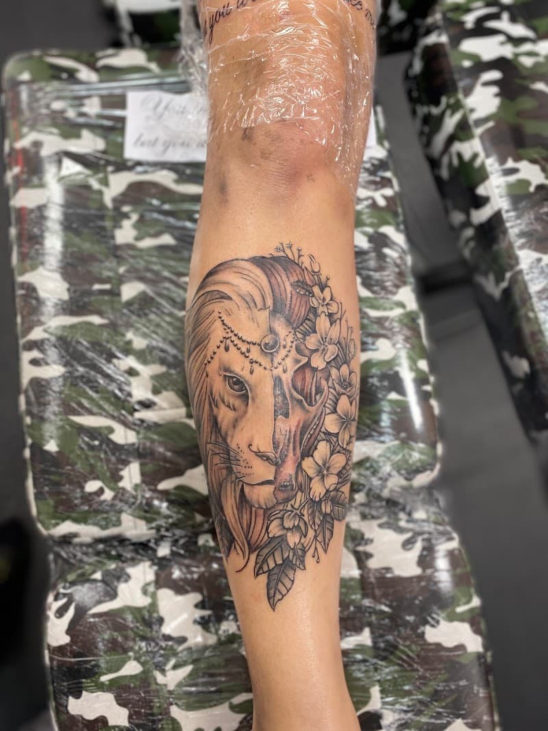 Halve leeuw, halve schedel met bloemen en sieraden op onderbeen.