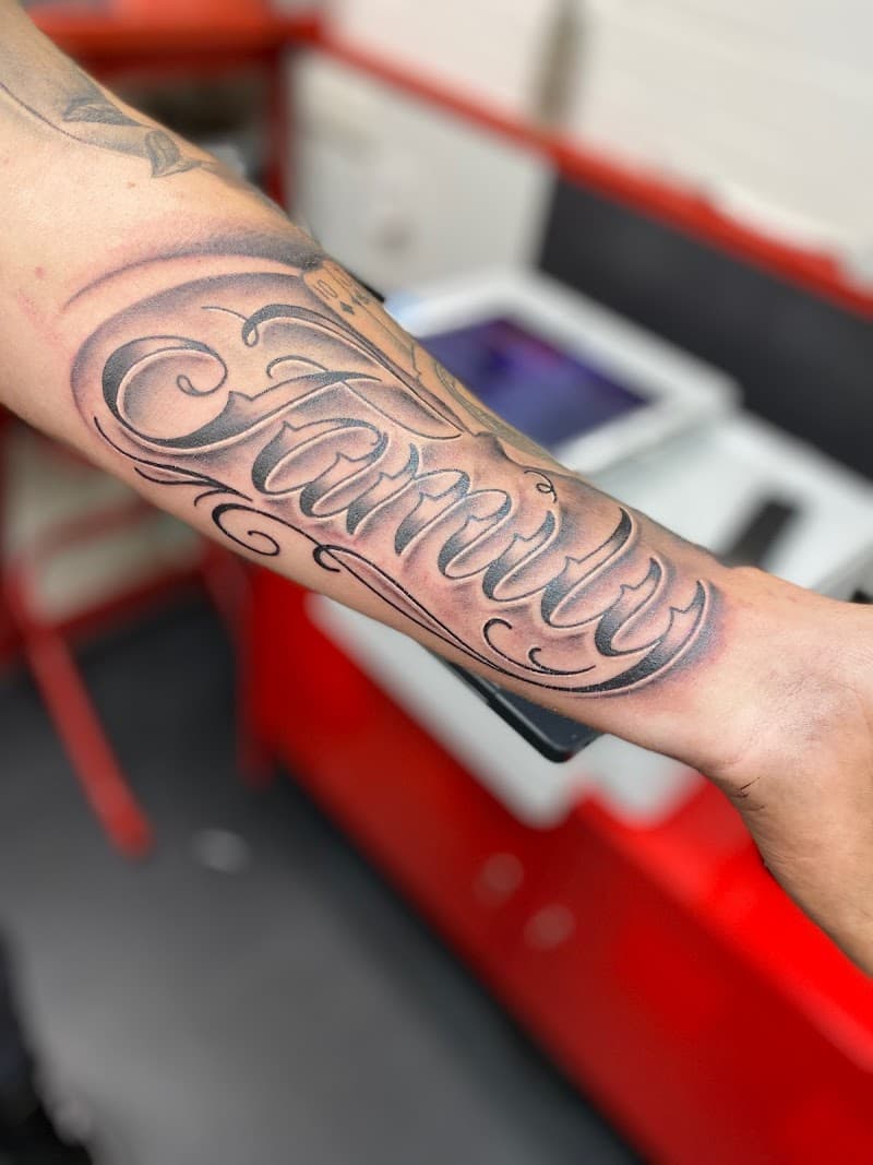 Zwart-wit 'Family' script tattoo op onderarm.