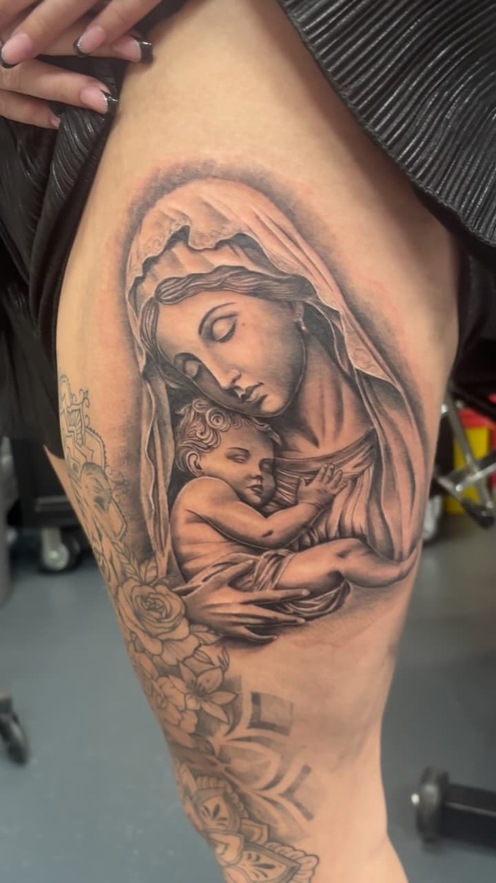 Realistische tattoo van Maria met kind op bovenbeen.
