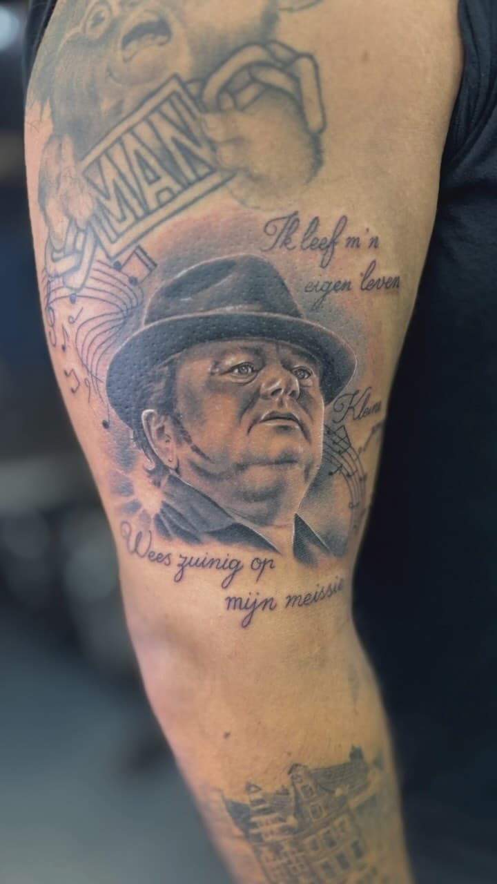 Realistisch portret van André Hazes met hoed en tekst op bovenarm.